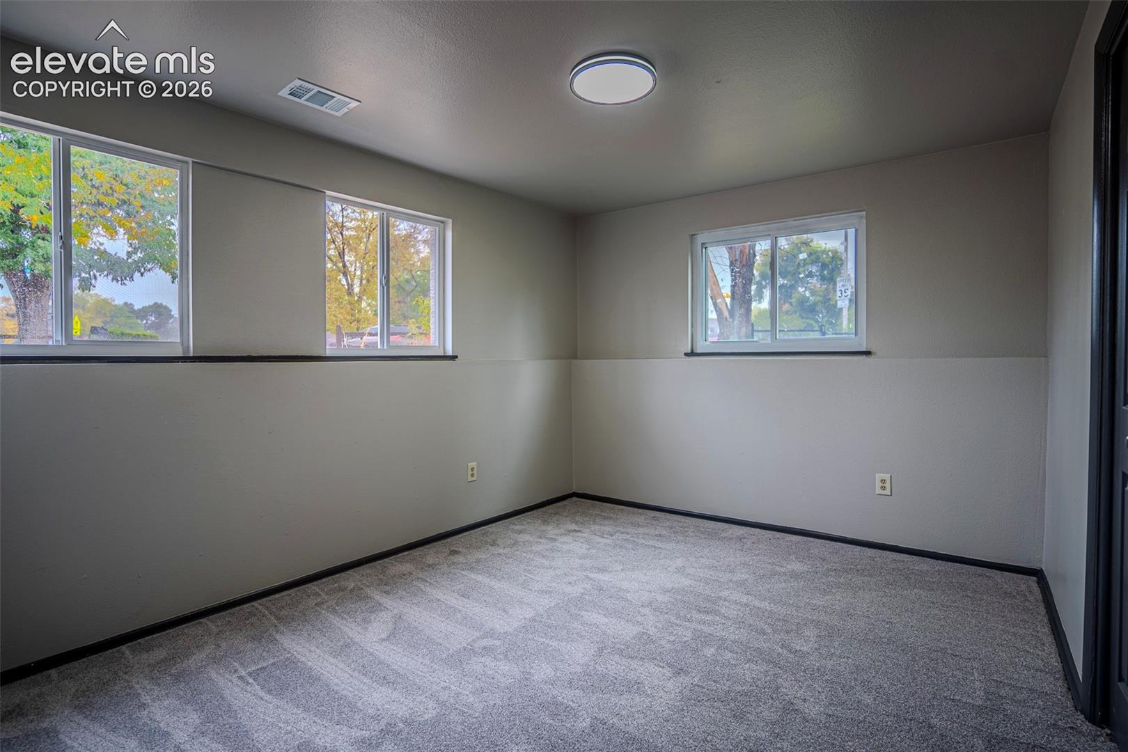Neutral-toned interior featuring wall-to-wall carpeting, three sliding windows, and a flush-mount overhead light fixture