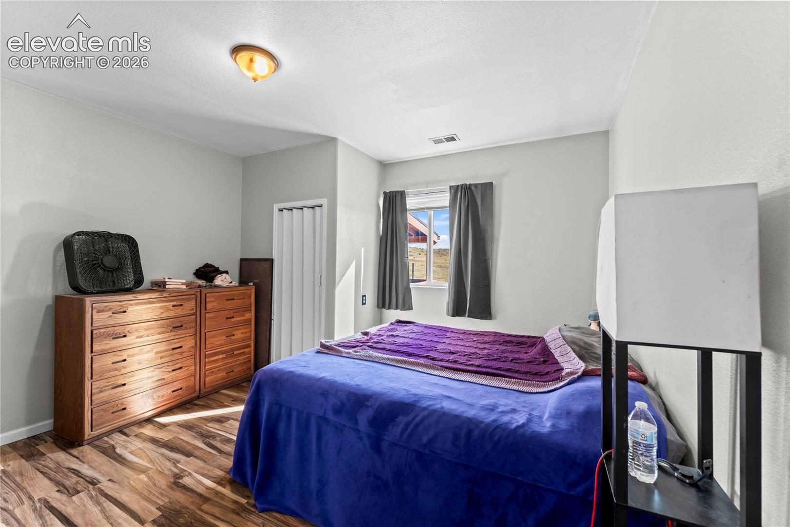 Bedroom featuring neutral paint, wood-finish flooring, a single window, and a folding-door closet