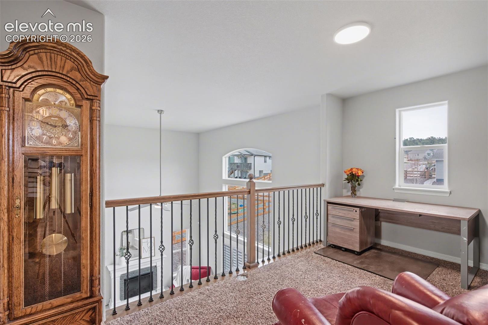 Carpeted loft area with iron baluster railing, wood top railing, and white window trim