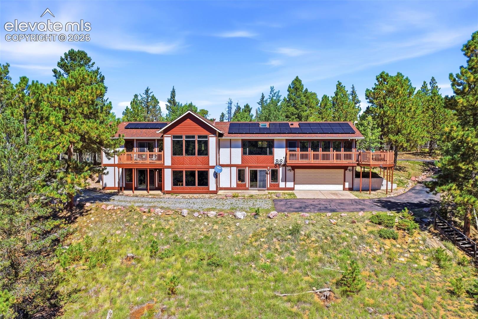 Multi-level exterior with extensive decking, integrated solar panels, and attached garage