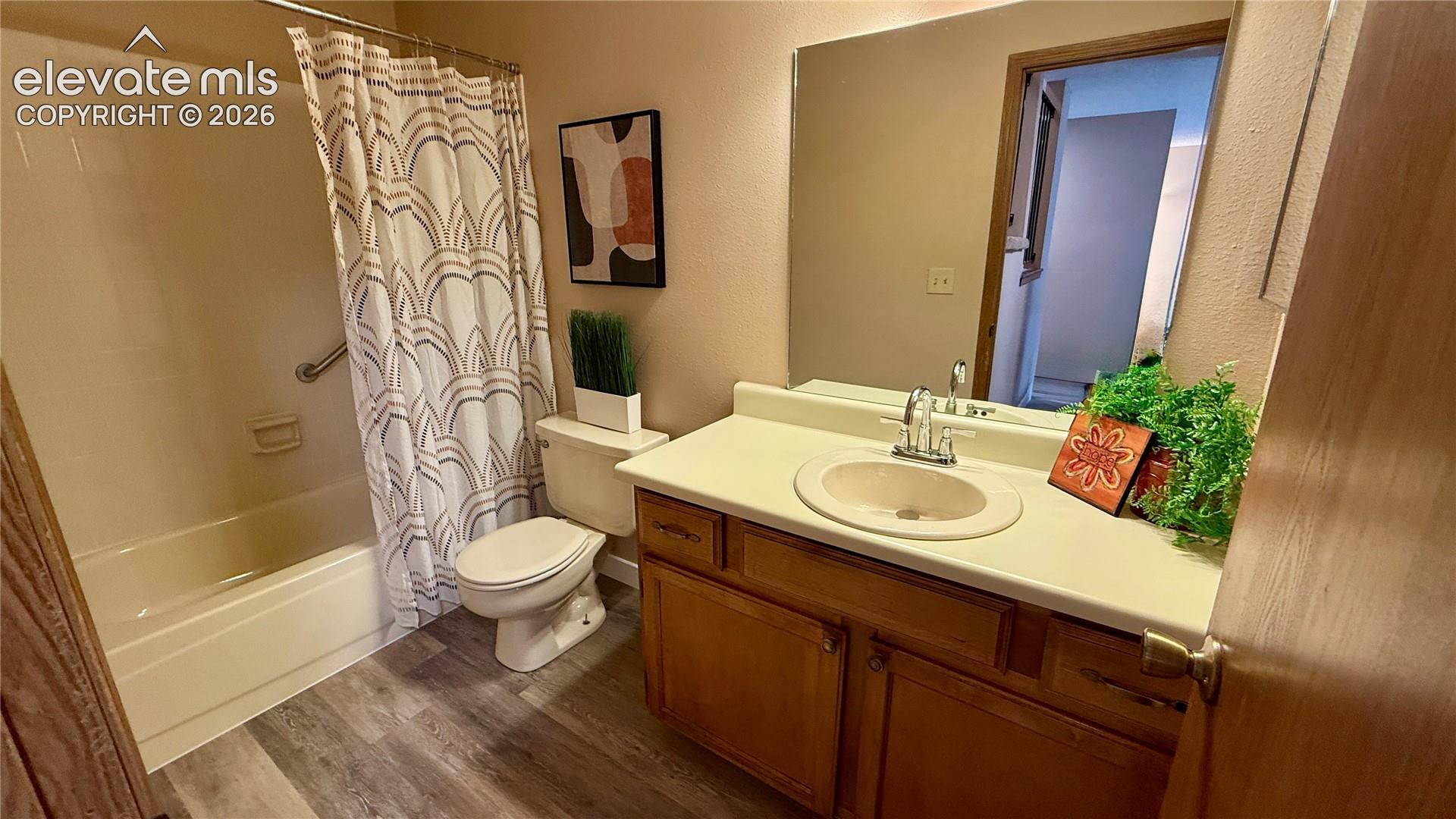 Bathroom featuring a wood-finish vanity with a molded countertop and integrated sink, a large wall-mounted mirror, a tub-shower combination with a tile surround, and wood-look flooring