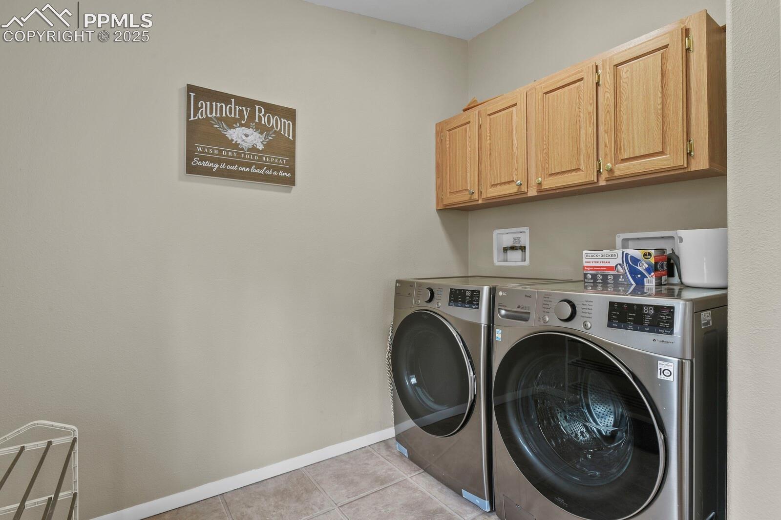 Washroom featuring light tile patterned flooring, washer and dryer, and cabinet space