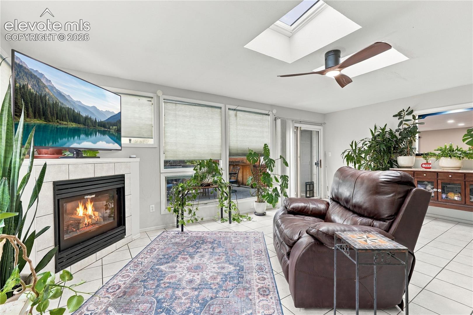 Ceramic tile flooring, fireplace with a tile surround, built-in wooden cabinetry, skylight, and a ceiling fan