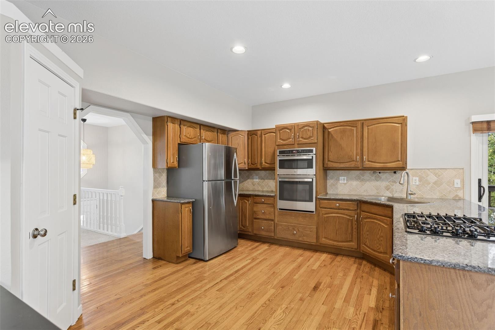 Wood-finish flooring with recessed lighting, wood cabinetry, stainless steel appliances, and stone countertops