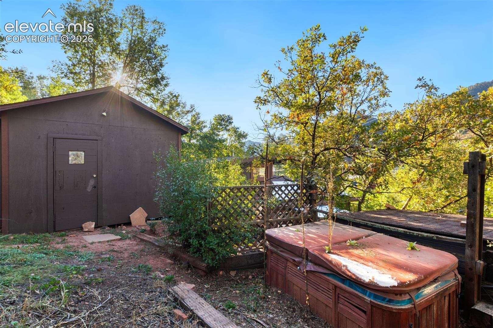 Outdoor space featuring a standalone storage structure, lattice fencing, and a built-in hot tub