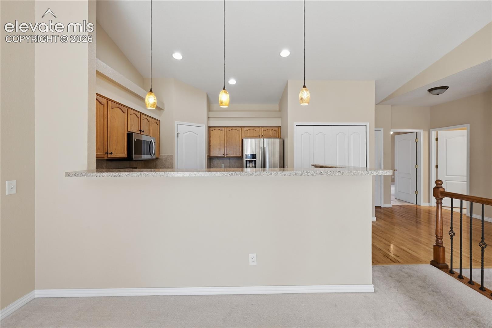 Kitchen featuring wood cabinetry, stone-surface breakfast bar, stainless steel appliances, and pendant lighting, with wood-finish flooring in the surrounding area