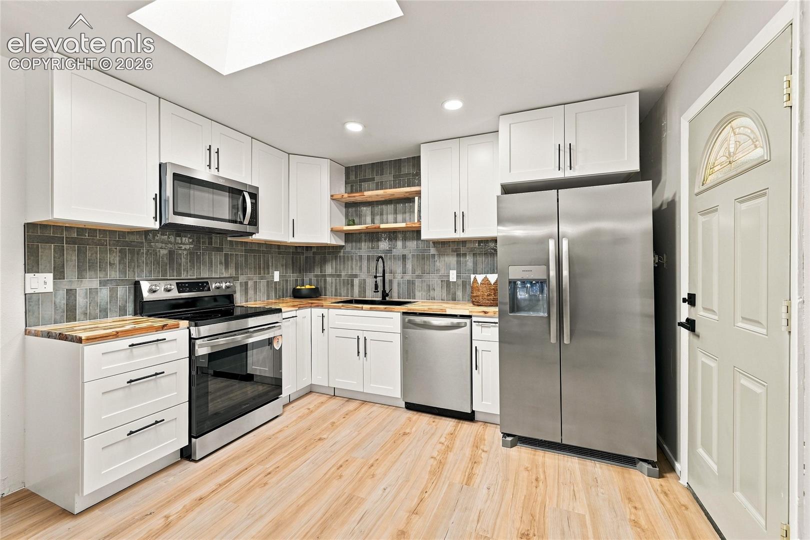White cabinetry, wood-finish countertops, stainless steel appliances, and a tiled backsplash