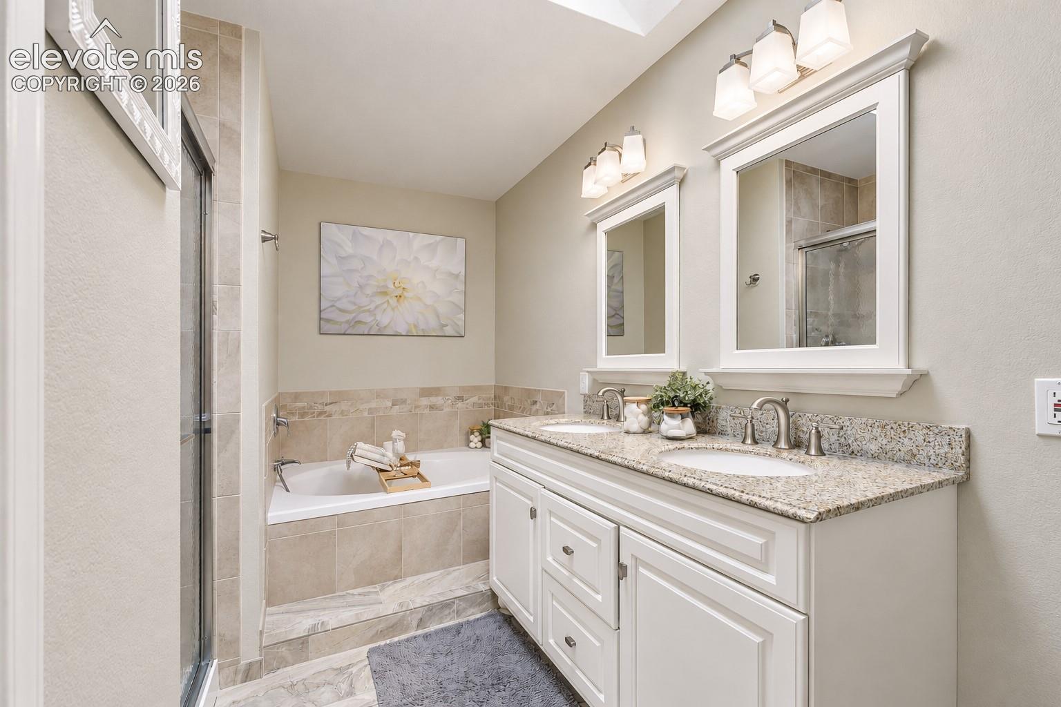 Primary Bathroom with dual sink vanity, granite countertops, framed mirrors, a soaking tub, and separate shower.