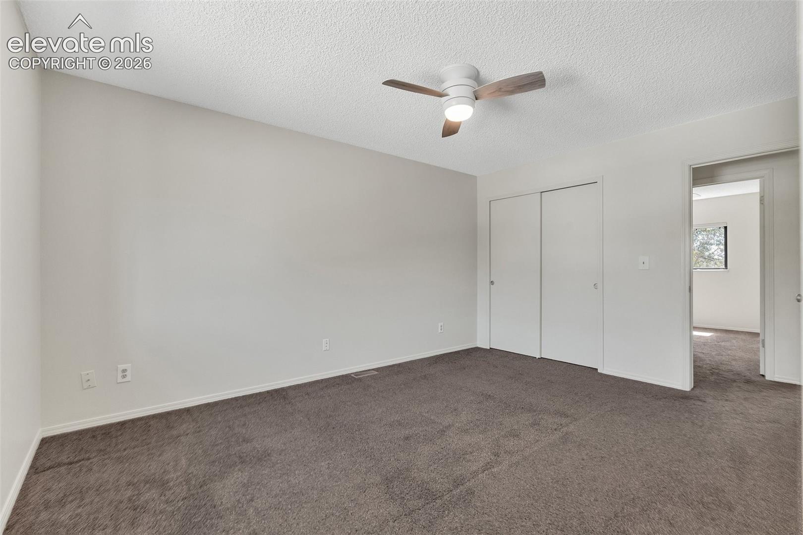 Neutral wall paint with textured ceiling, ceiling fan with integrated lighting, and carpet flooring