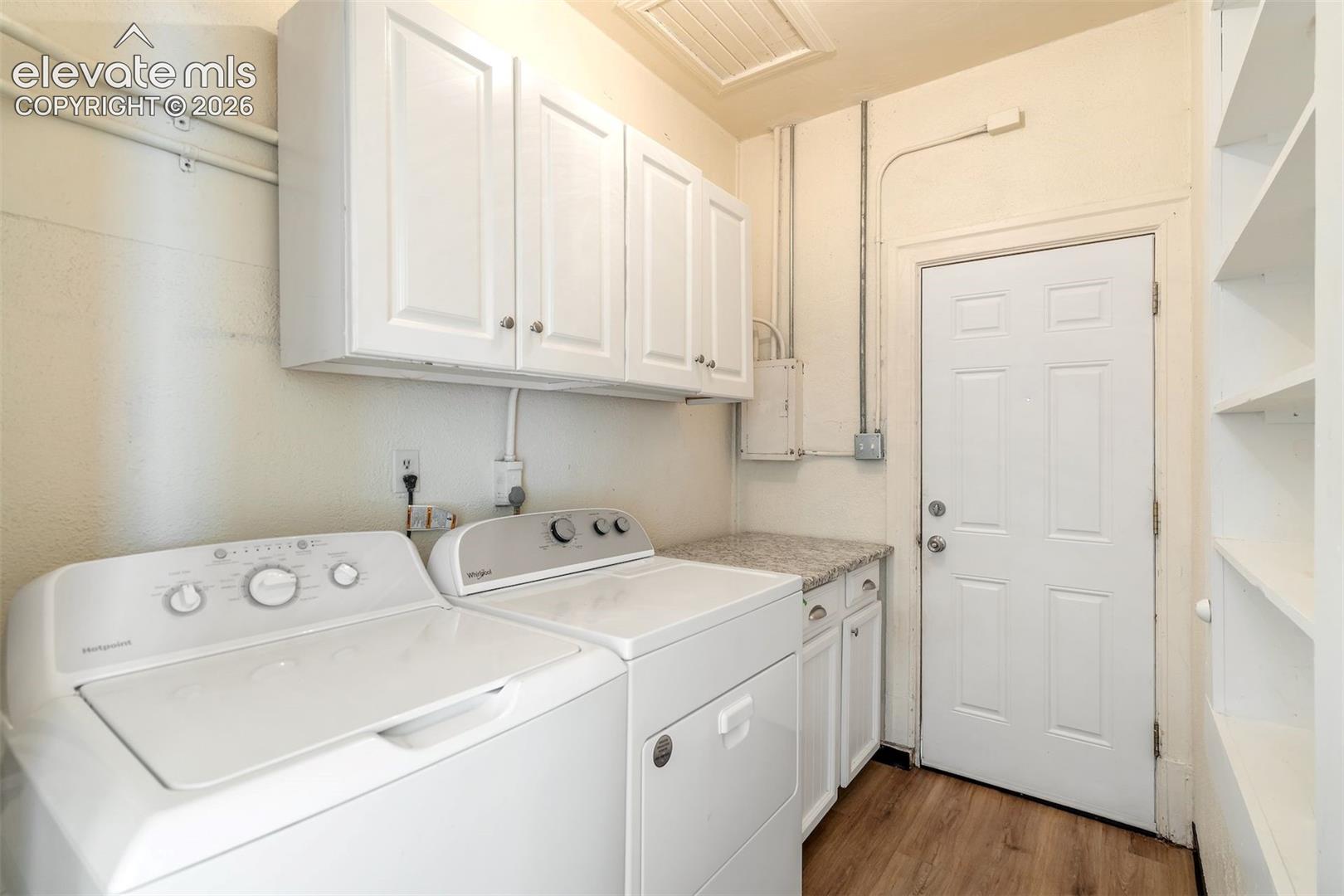 Laundry area featuring wood-finish flooring, white cabinetry, a stone-composite countertop, and built-in wall shelving