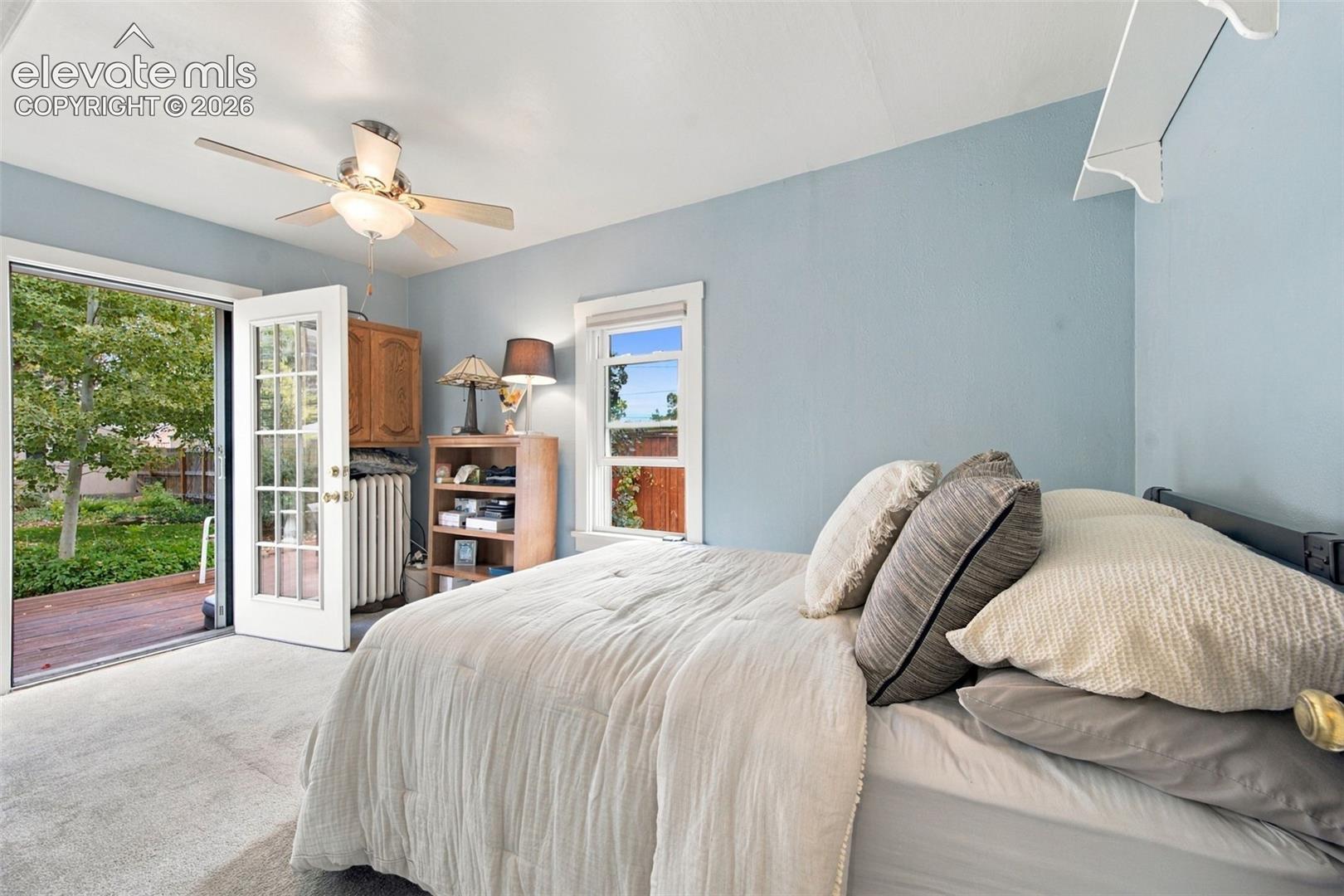 Bedroom featuring neutral carpeting, a ceiling fan, a window, and a full-light glass door opening to a deck