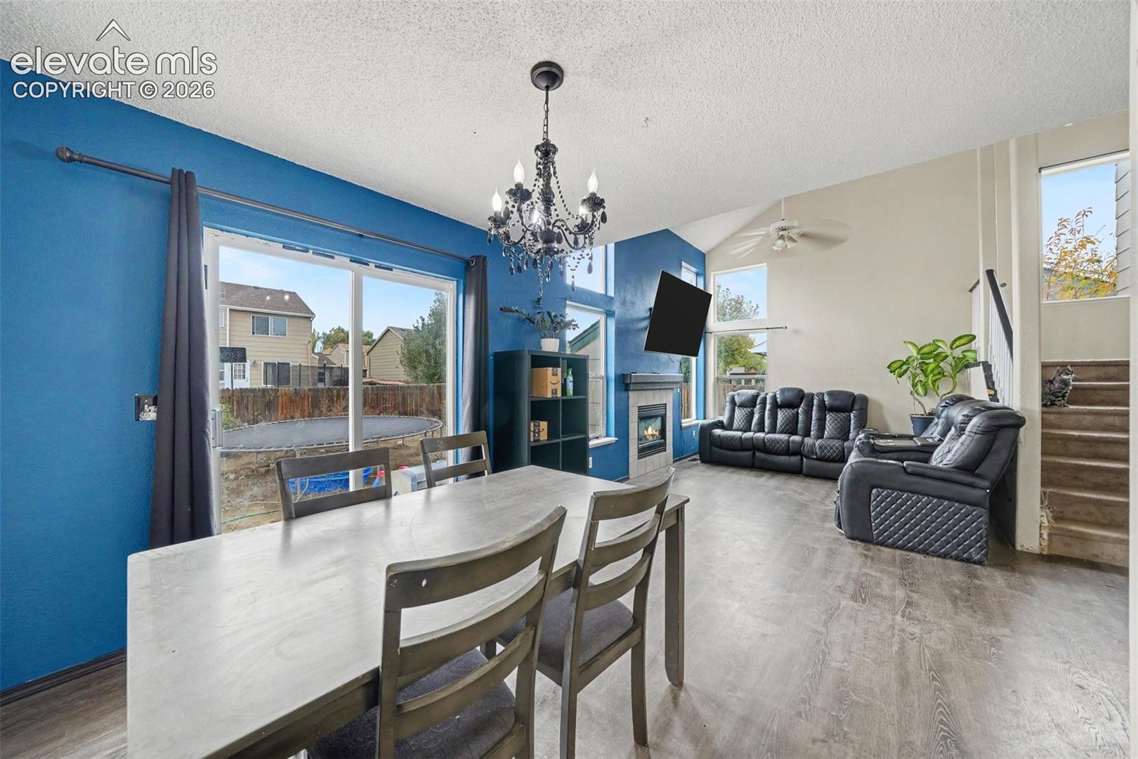 Open-concept living space featuring vaulted ceilings, a focal-point gas fireplace, wood-finish flooring, sliding glass door, and a decorative chandelier