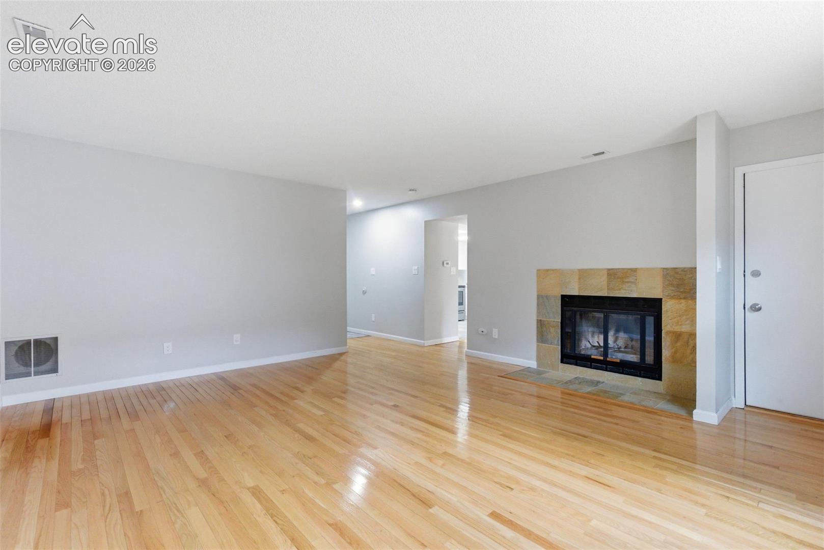 Living area featuring wood-finish flooring, light gray wall paint, and a fireplace with a stone-tile surround