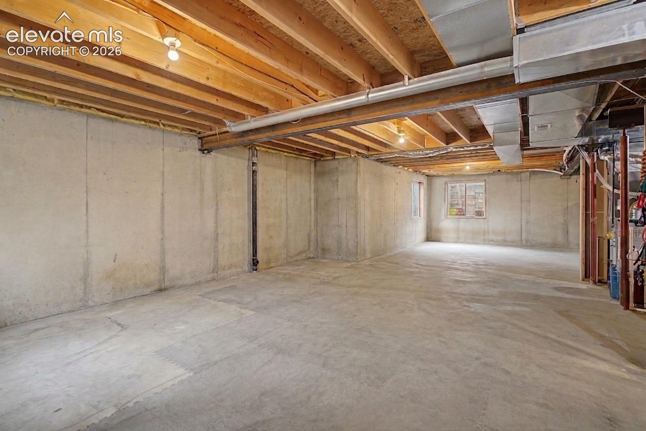Expansive unfinished basement featuring concrete flooring and walls, exposed wood ceiling joists, and integrated ceiling lighting