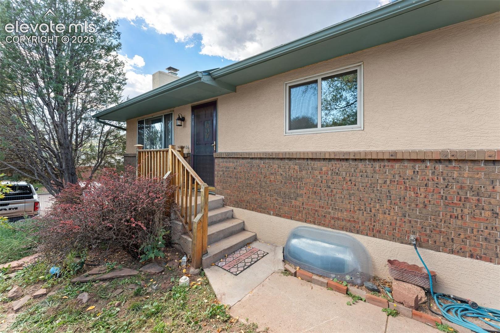 Stucco and brick exterior with a dark entry door, concrete steps, and a wooden handrail