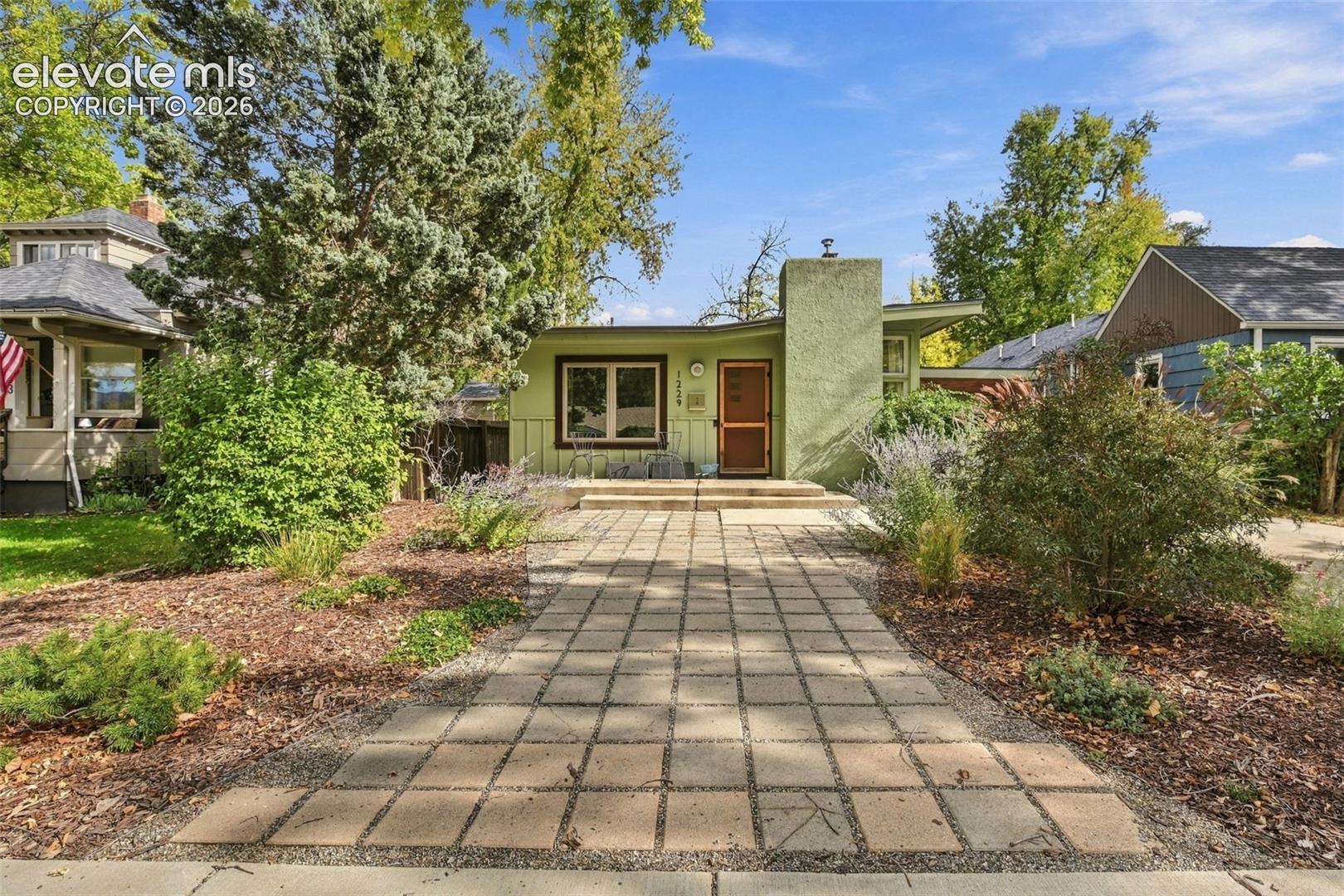 Stucco exterior featuring a prominent masonry chimney, concrete paver walkway, and mature landscaping
