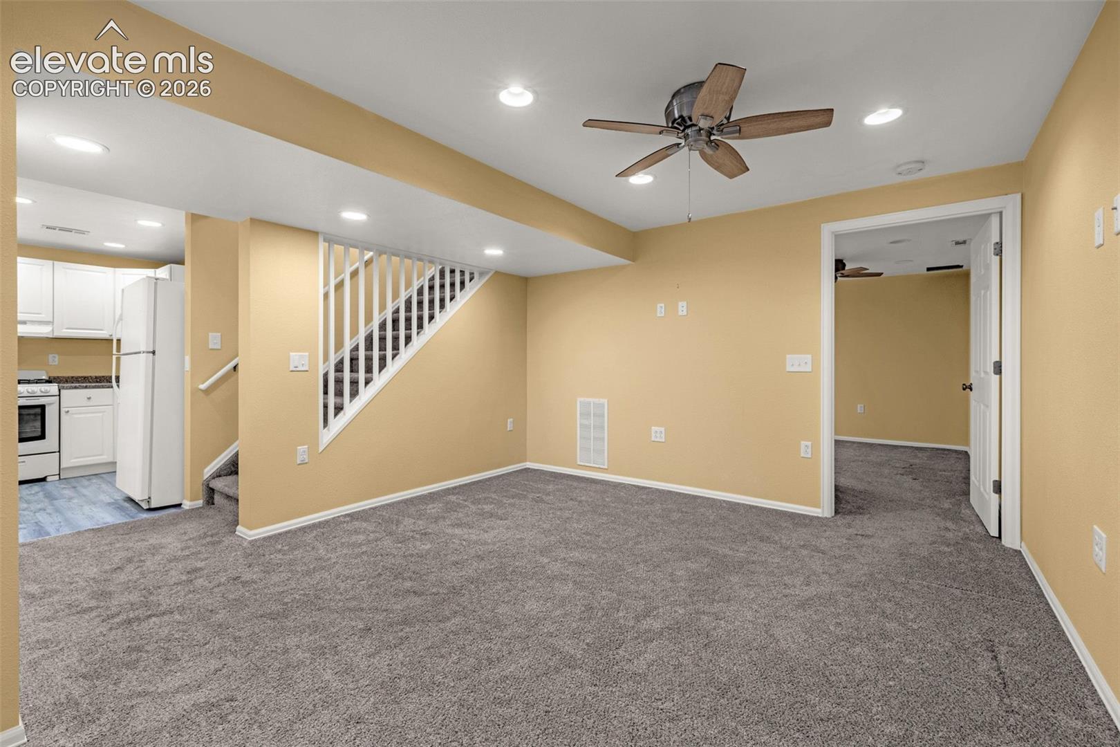 Open-concept interior featuring wall-to-wall carpeting, recessed ceiling lighting, a ceiling fan with integrated light, and a staircase with white balusters