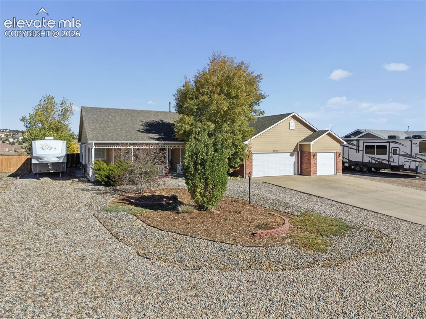 Single-story residence featuring a covered front porch, attached three-car garage, brick facade accents, and low-maintenance gravel landscaping