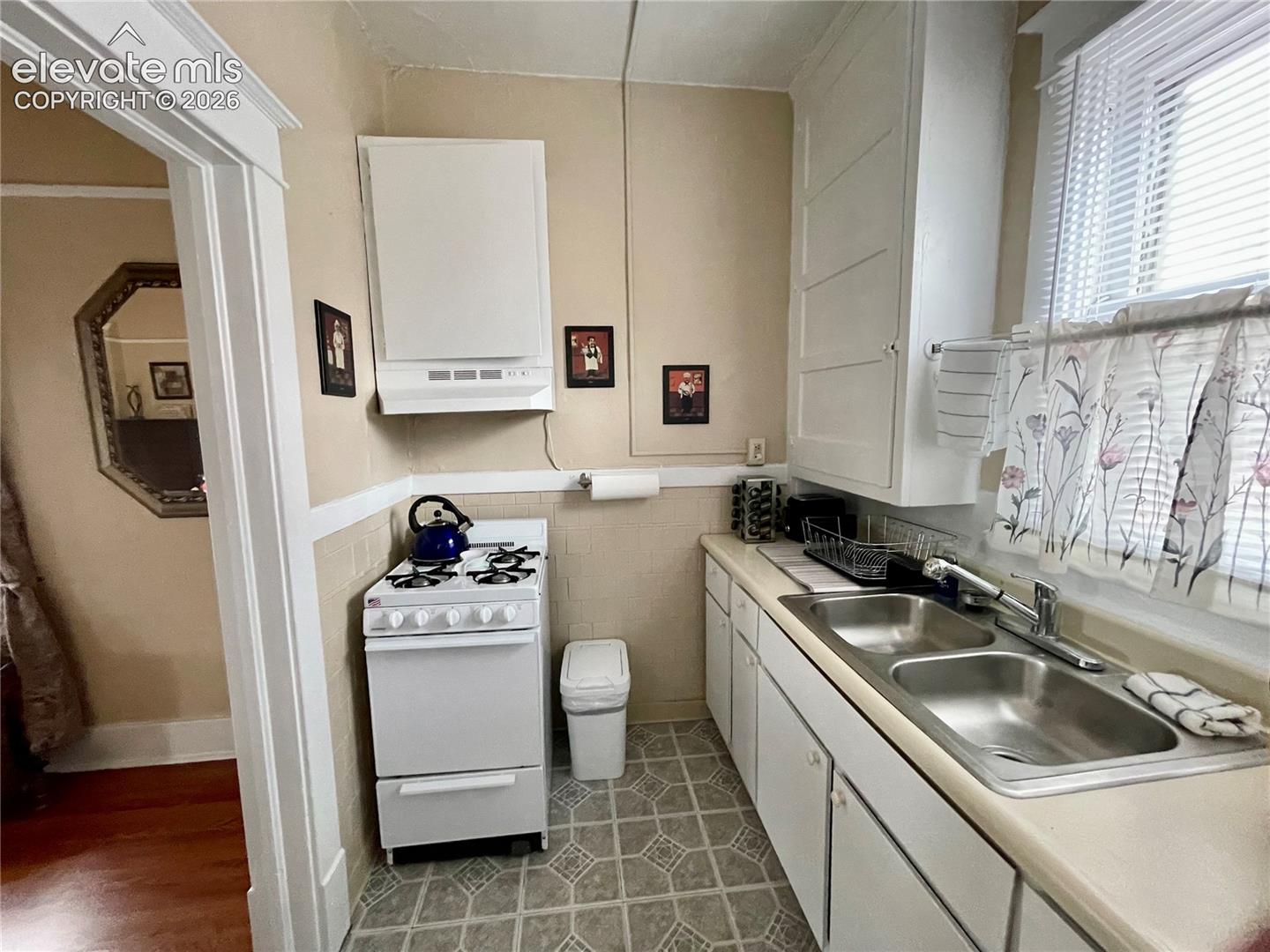White cabinetry, dual basin stainless steel sink, gas range, and patterned flooring
