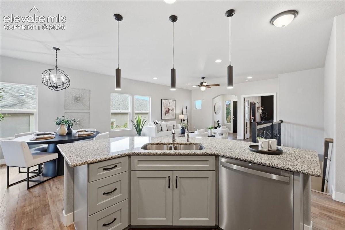 Kitchen island with integrated stainless steel sink, light-toned countertop, light gray cabinetry, and pendant lighting