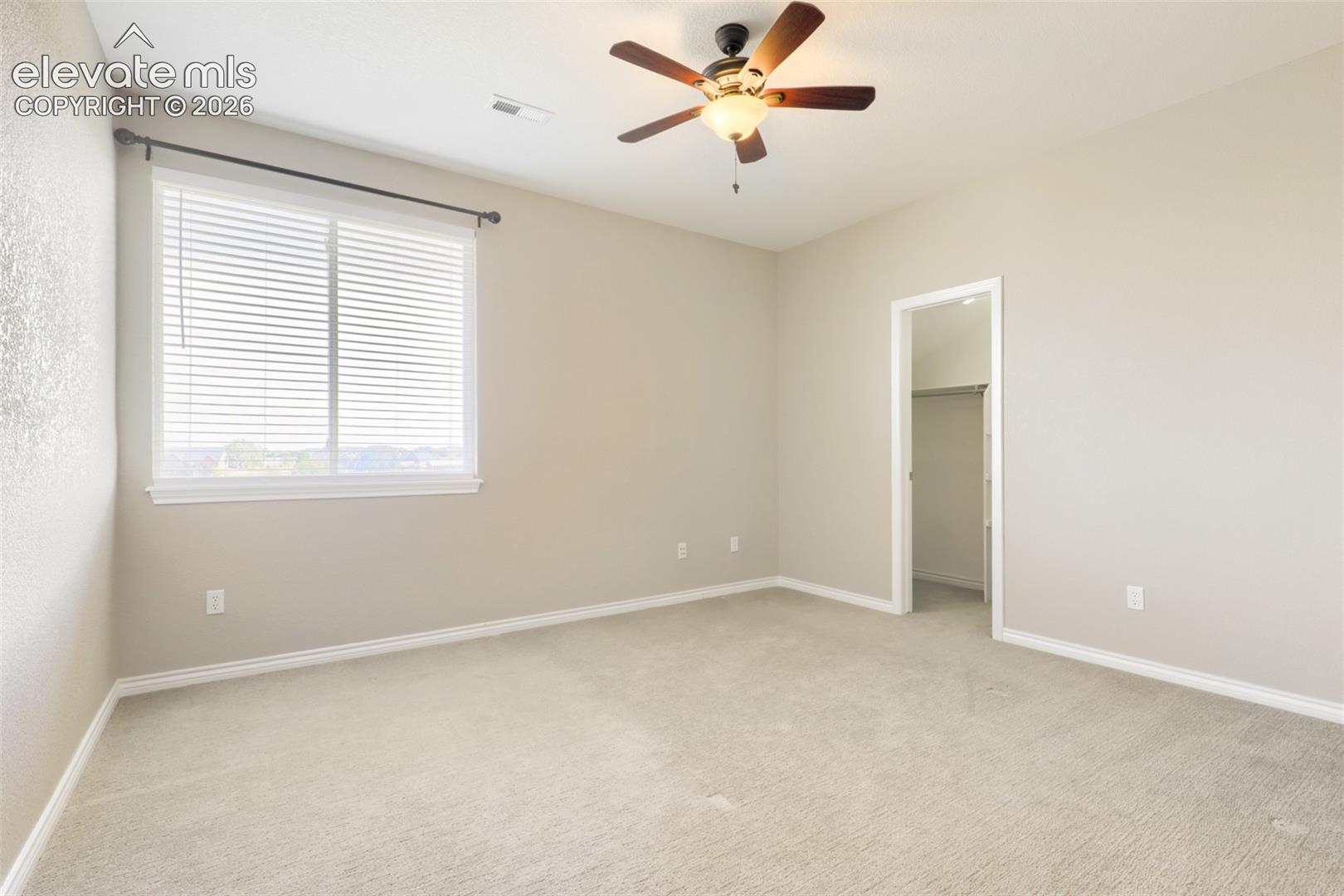 Spacious second-floor bedroom complete with wall-to-wall carpeting, a ceiling fan, a bright window with blinds, and a private walk-in closet.
