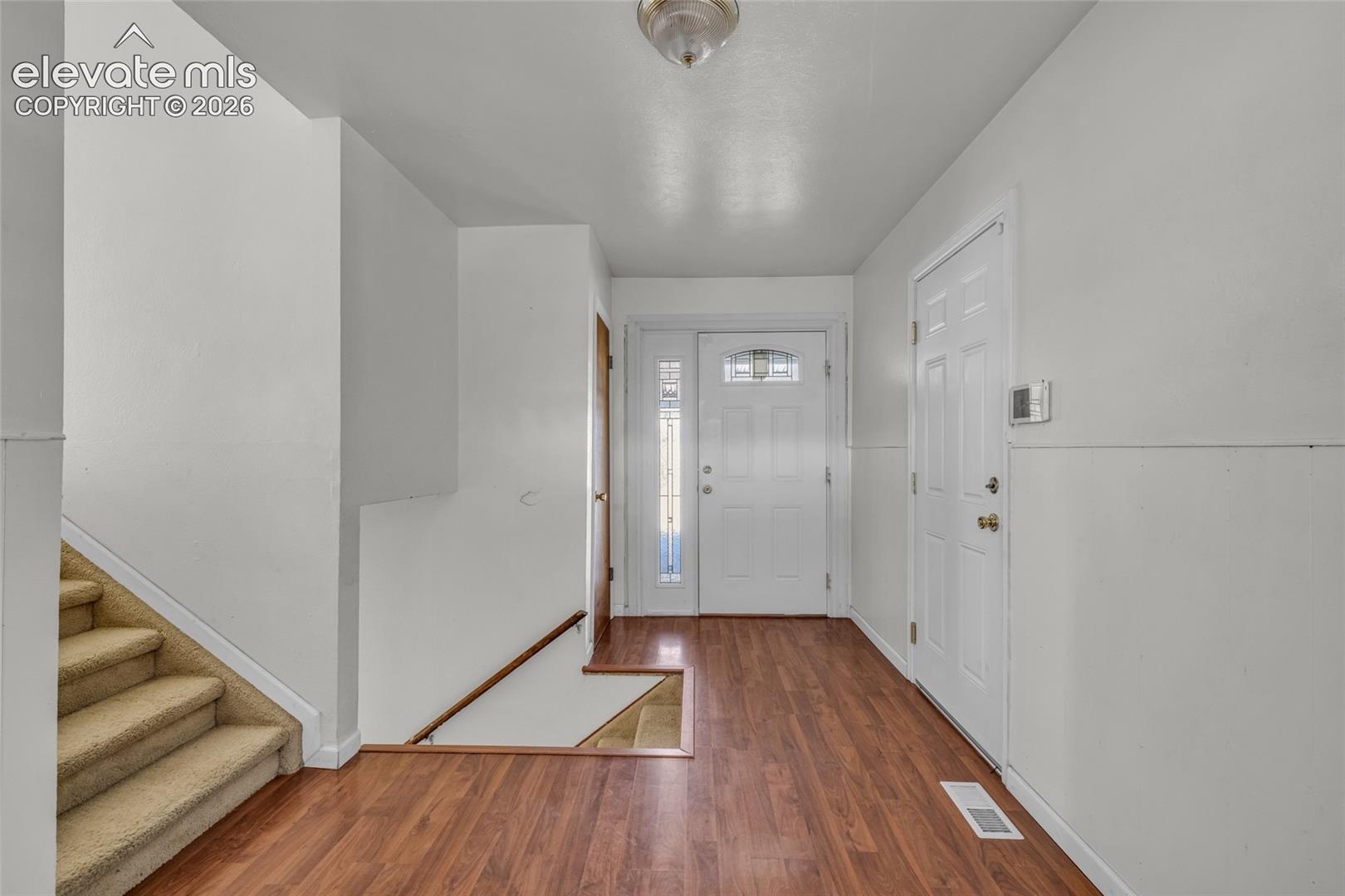 Entryway featuring wood-finish flooring, two panel doors, and a carpeted staircase