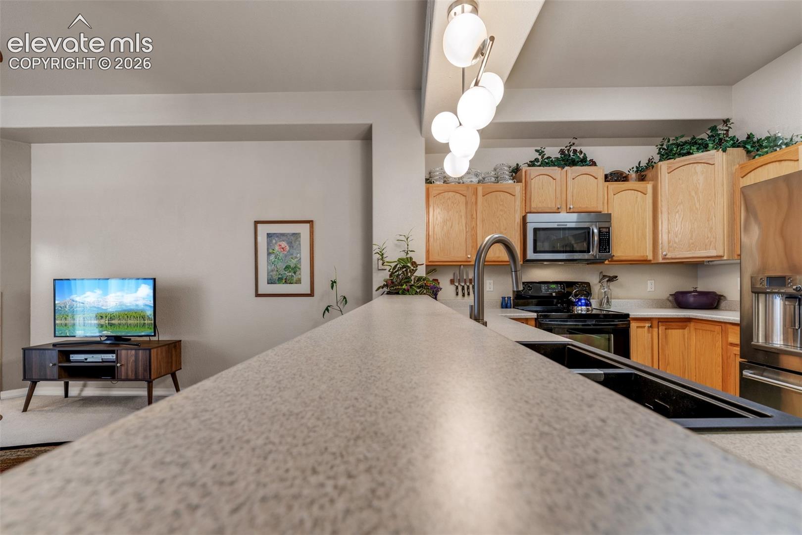 Kitchen featuring light wood cabinetry, white countertops, stainless steel microwave, black electric range, and a double basin sink with a gooseneck faucet