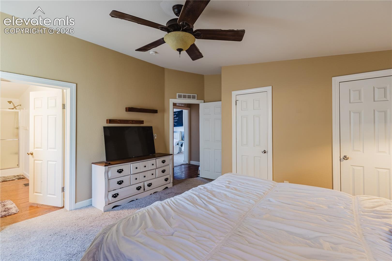 Vaulted ceiling with a ceiling fan, carpet flooring, multiple panel doors, and warm-toned wall paint