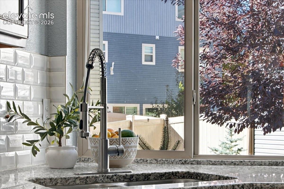 Granite-look countertop, white subway tile backsplash, stainless steel pull-down faucet, and large window