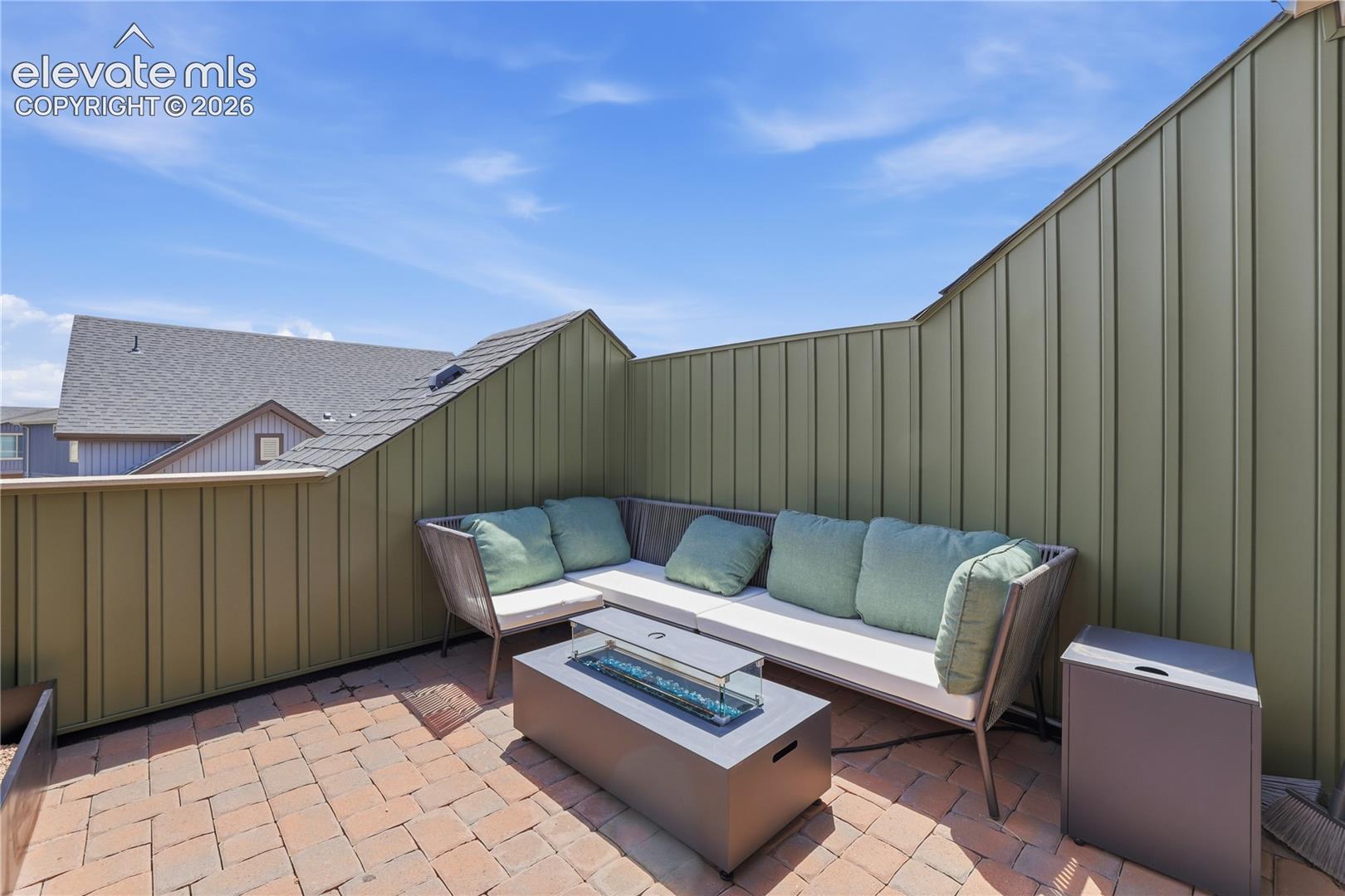 Private rooftop patio featuring brick paver flooring, board-and-batten style privacy walls, and a built-in fire pit