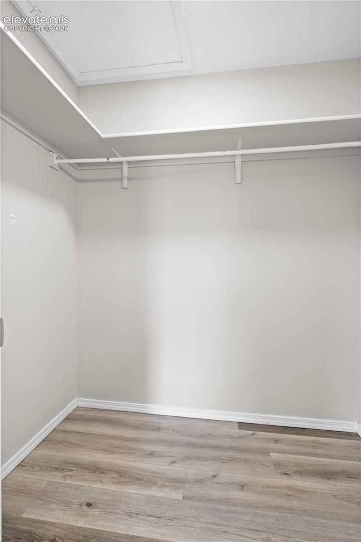 Walk-in storage area featuring wood-finish flooring and built-in shelving with integrated clothing rods