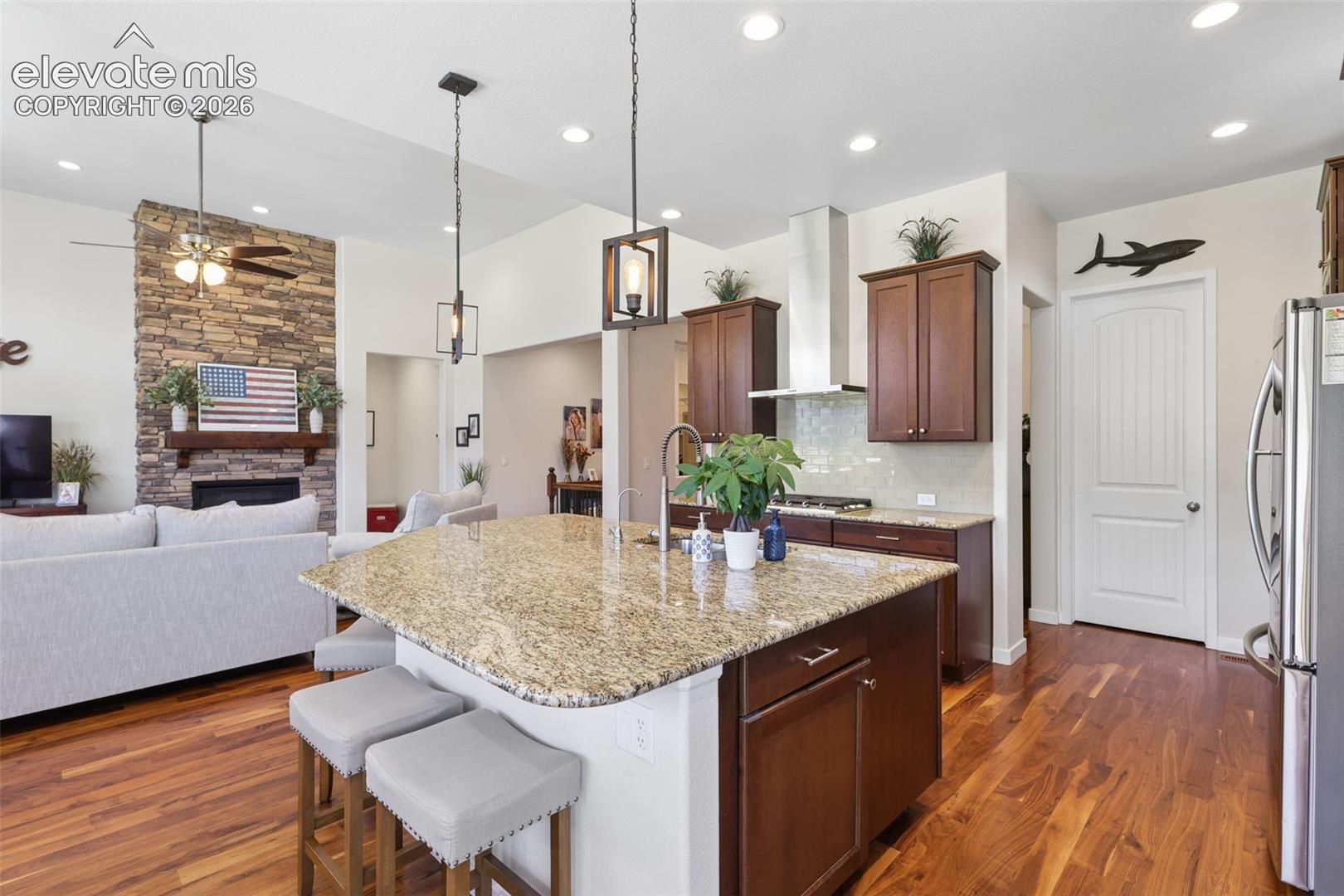 Kitchen featuring a granite-topped island with seating, pendant lighting, stainless steel range hood, and wood-finish flooring
