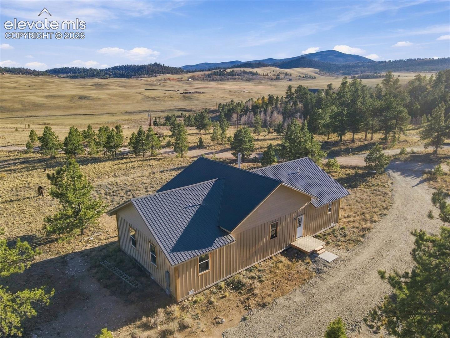 Single-story residence featuring vertical siding, a metal roof, and an expansive rural landscape with mountain scenery