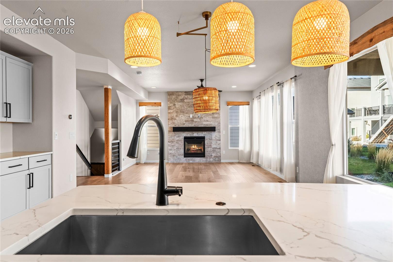 Kitchen featuring a quartz countertop, undermount stainless steel sink, and matte black pull-down faucet, highlighted by woven pendant lighting and a stone-clad fireplace
