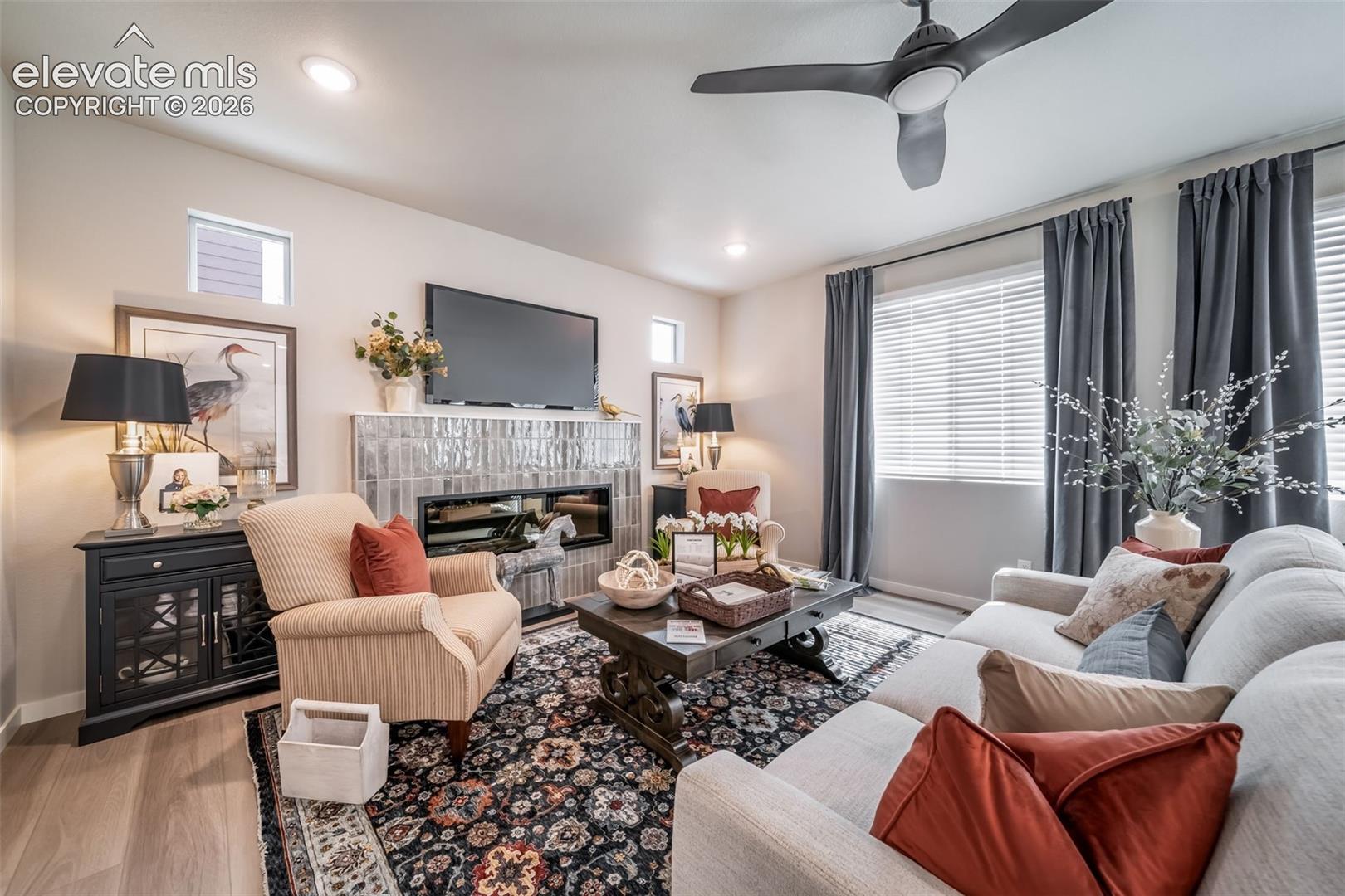 Living area featuring a modern linear fireplace with a textured tile surround, wood-finish flooring, recessed lighting, and a ceiling fan
*Photos of a model home*