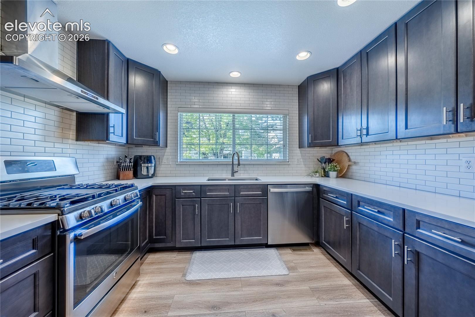 Kitchen featuring dark cabinetry, stainless steel appliances, white subway tile backsplash, light-toned countertop, and wood-finish flooring