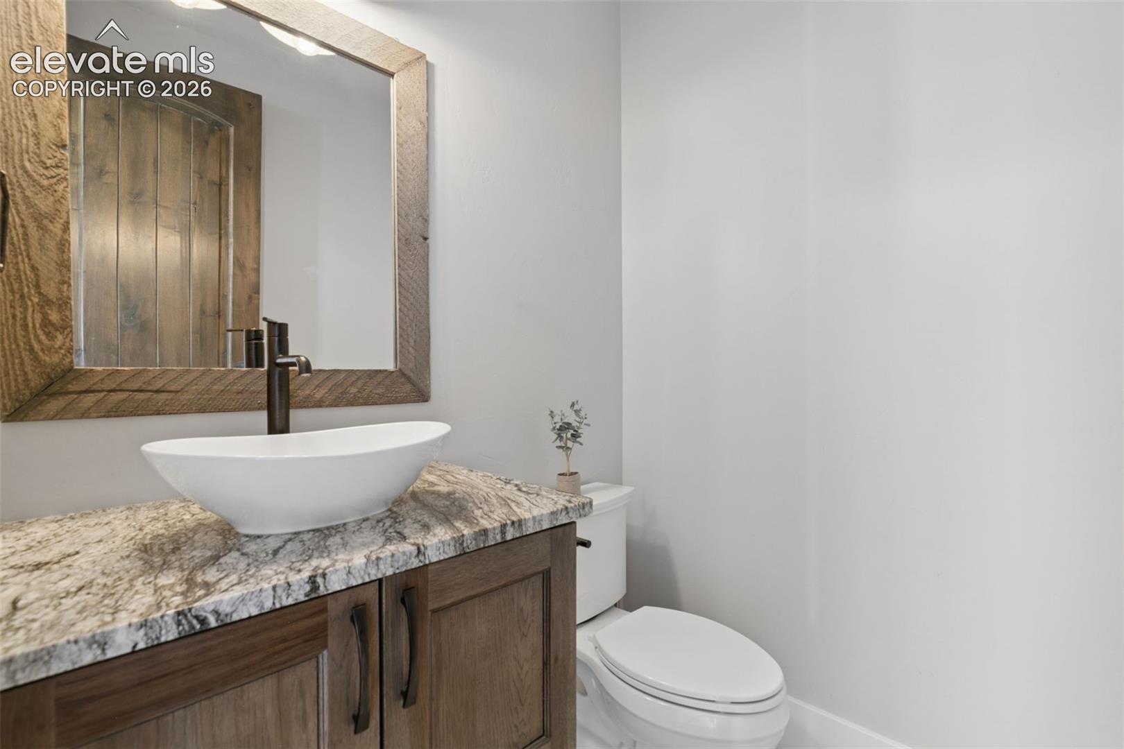 Wood-finish vanity with a vessel sink, stone countertop, and oil-rubbed bronze faucet