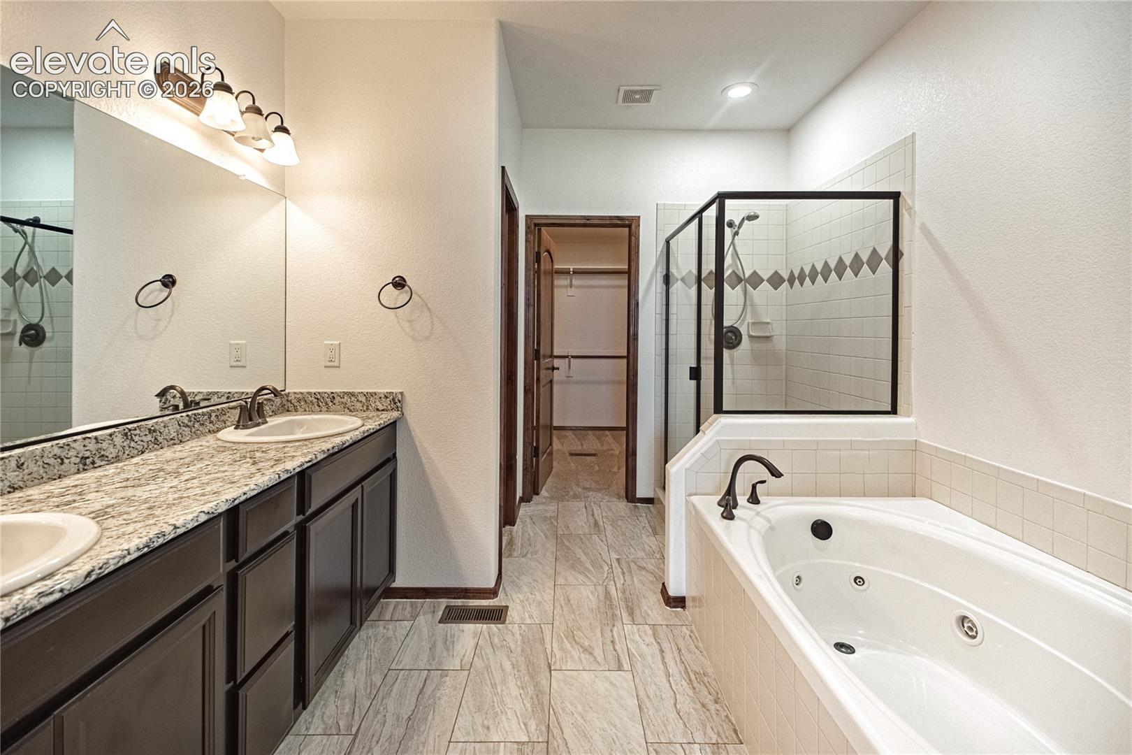 Bathroom featuring a double vanity with granite countertop, individual sinks, and dark cabinetry