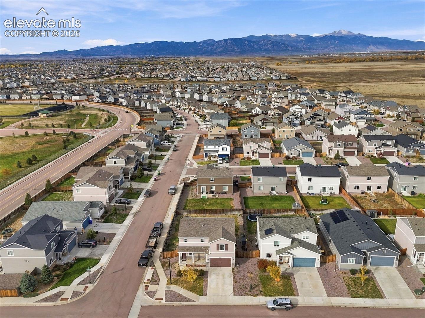Aerial perspective featuring a residential community with paved streets, detached single-family dwellings, and a prominent mountain range backdrop