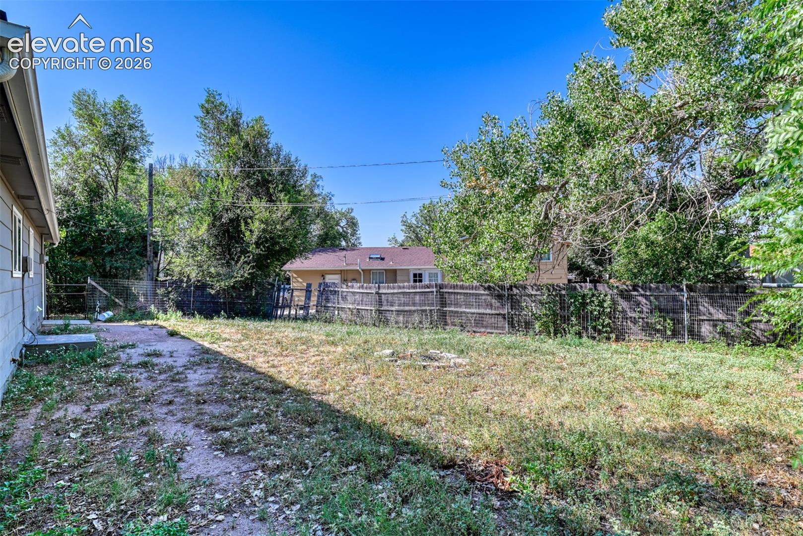 Expansive rear yard featuring a wooden privacy fence, mature trees, and a concrete patio pad