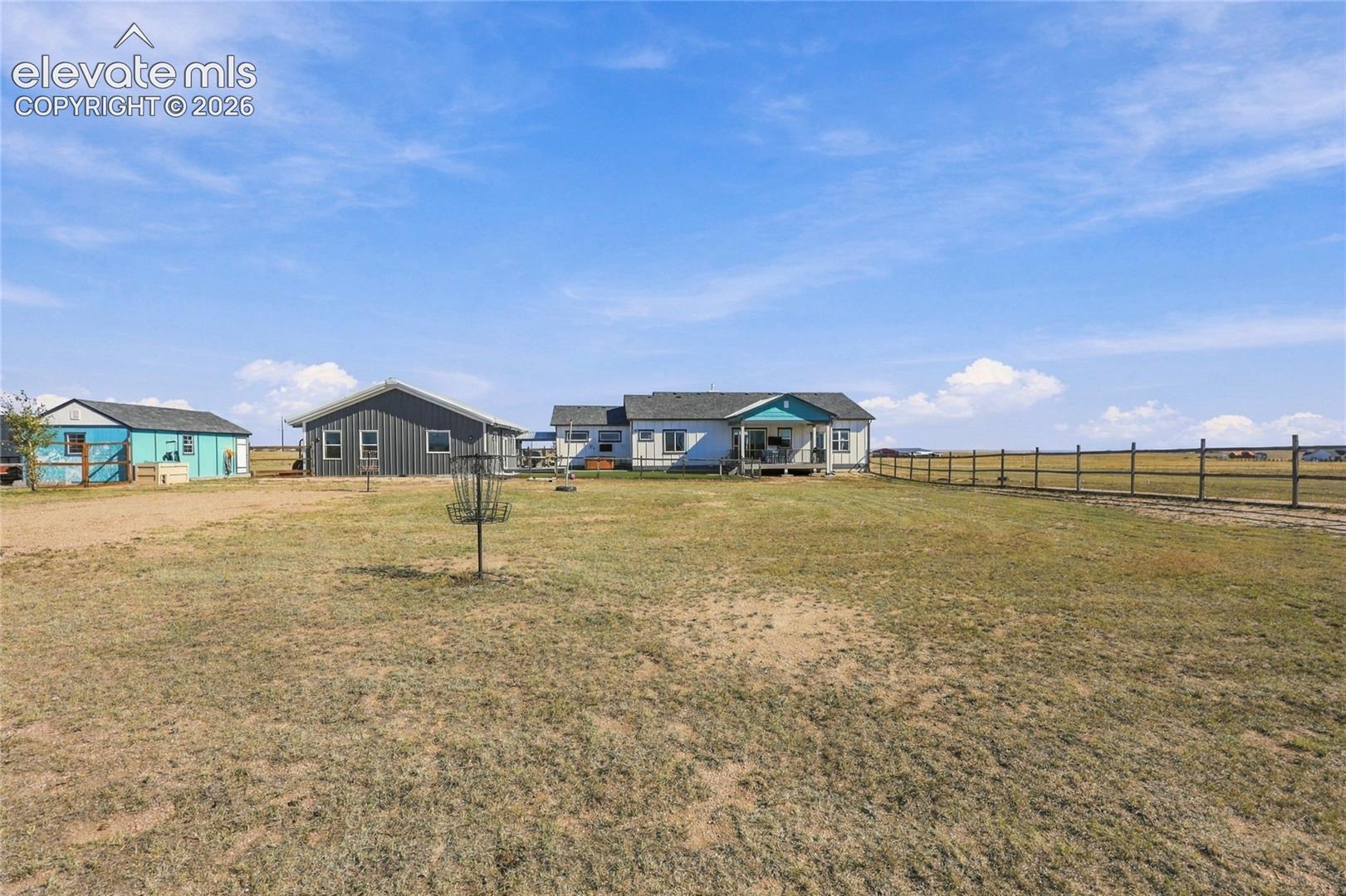 Expansive lot featuring a primary residence, detached workshop with metal siding, additional outbuilding, and perimeter post-and-rail fencing