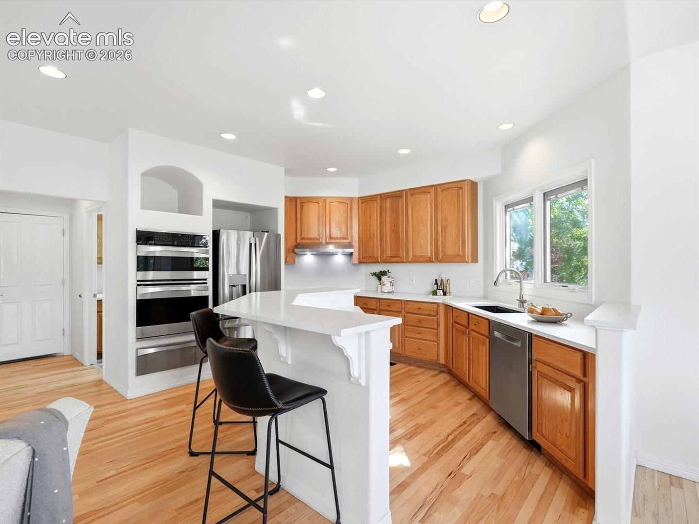 Kitchen featuring wood cabinetry, solid-surface countertops, built-in double ovens, recessed lighting, and wood-finish flooring