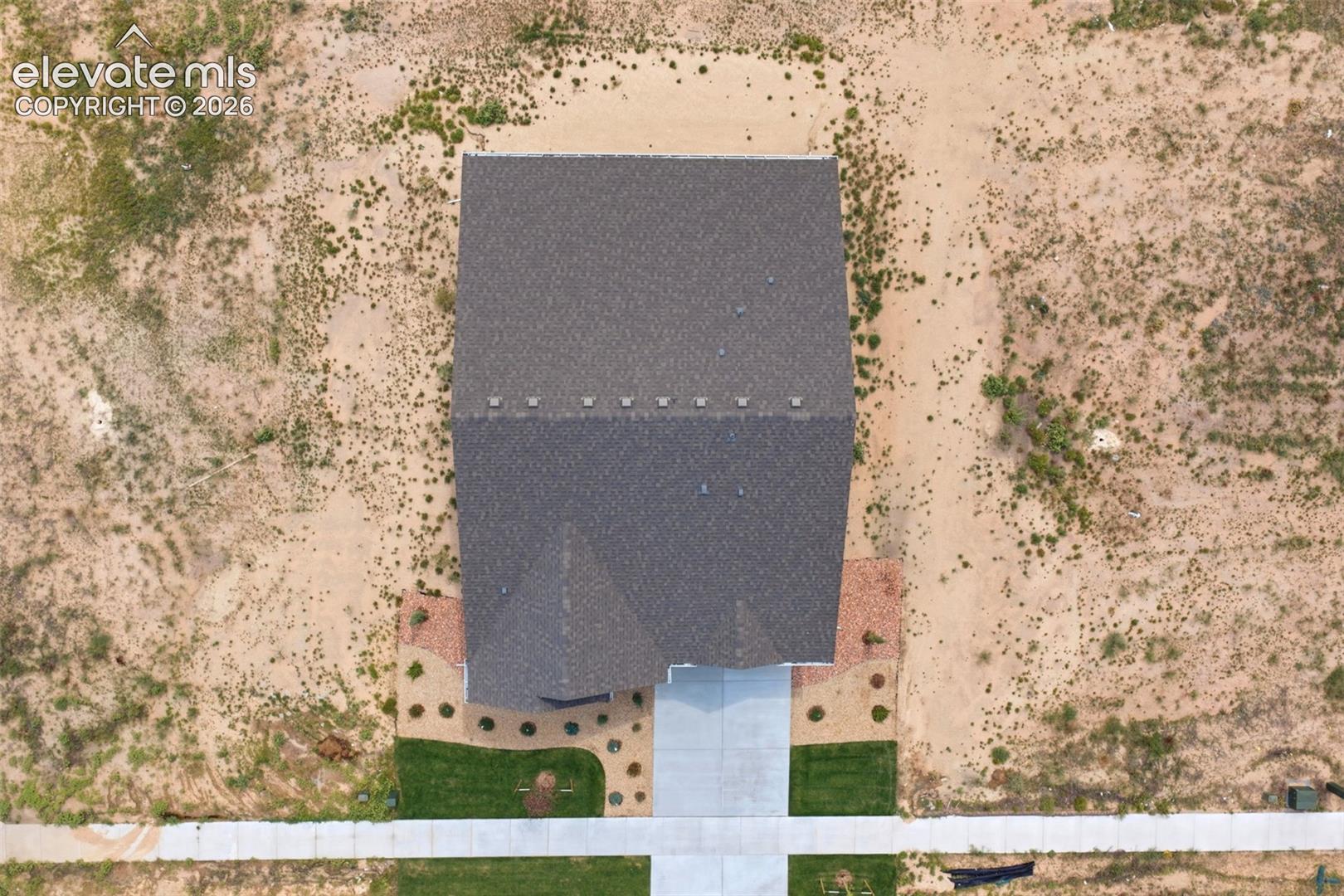 Aerial perspective of the property featuring a dark-toned asphalt shingle roof, concrete driveway, and established front lawn landscaping