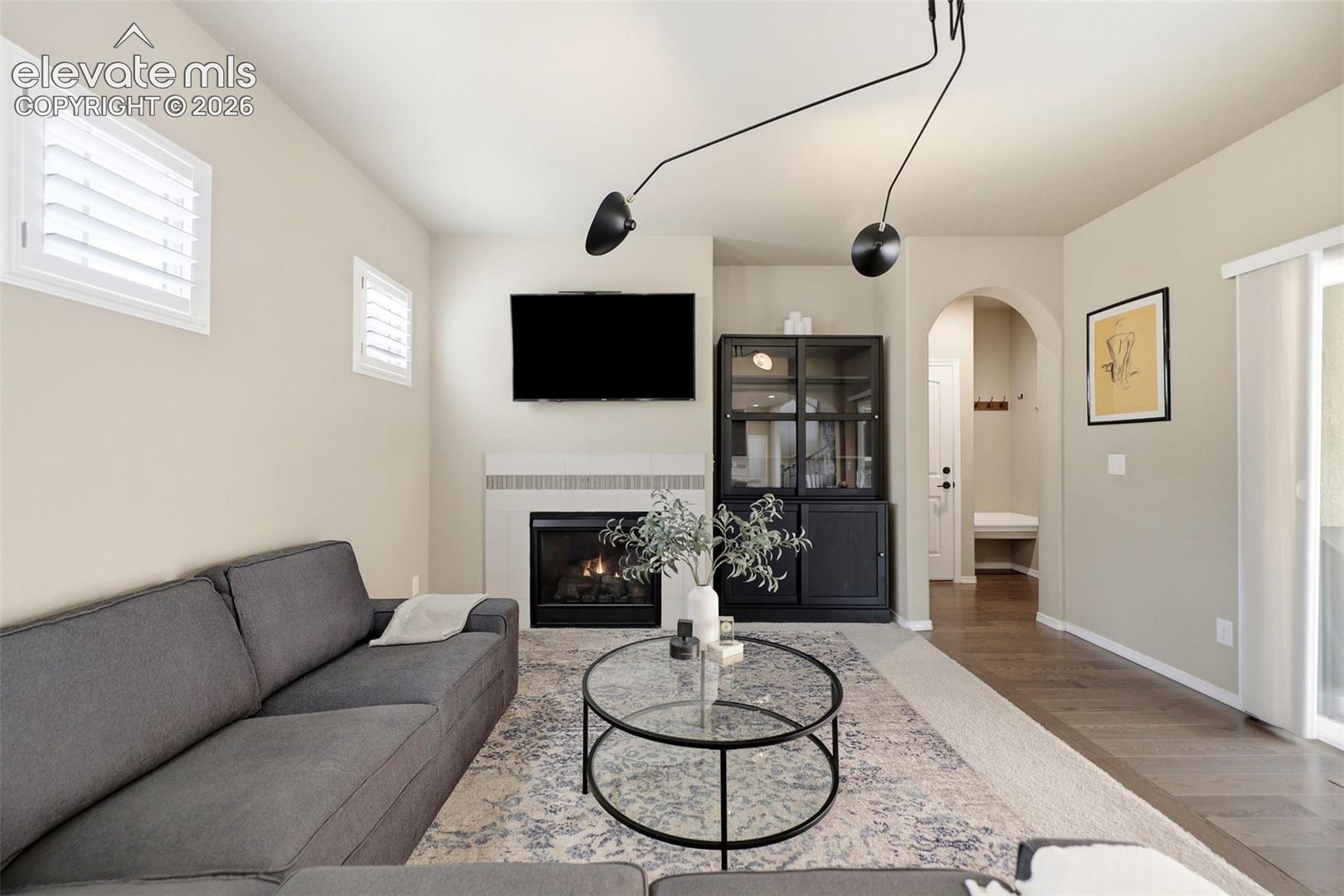 Fireplace with mantel, cabinetry, wood flooring, sliding glass door, and arched doorway