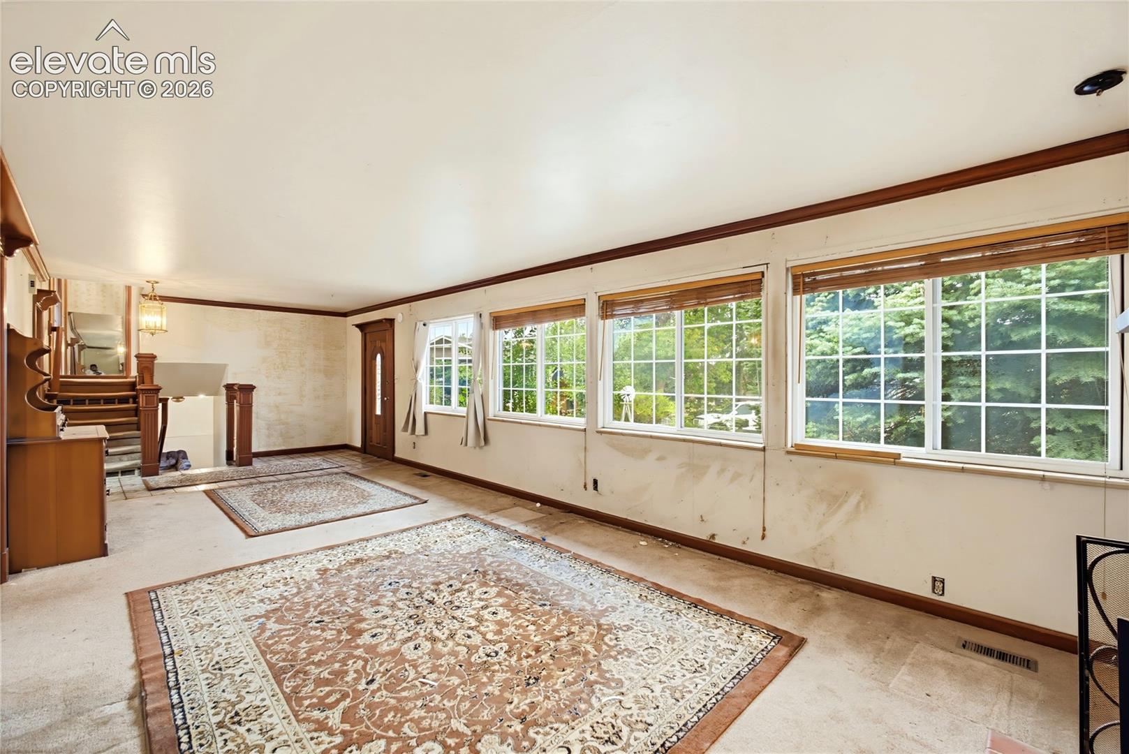 Spacious room with multiple grid-paned windows, wood trim, and a built-in staircase with wood banister