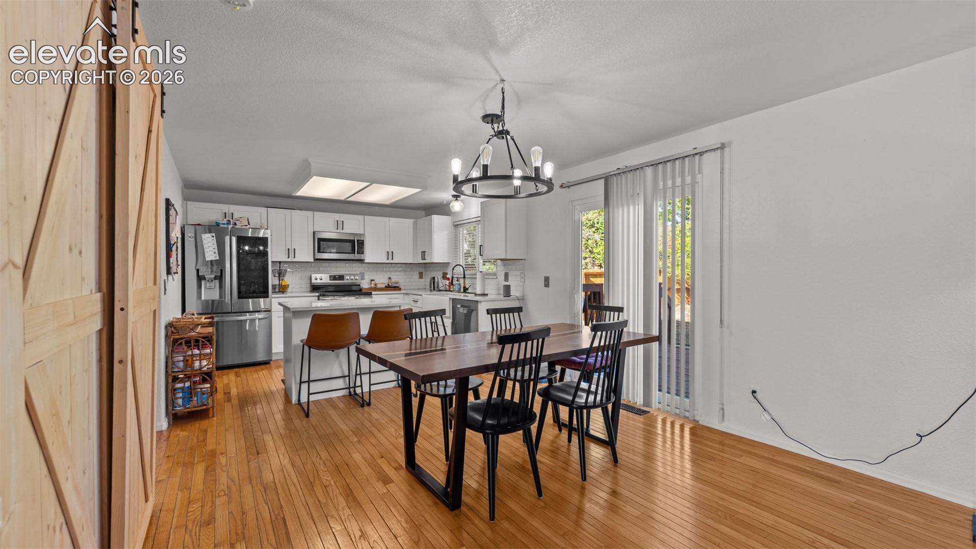 Open-concept kitchen and dining area featuring hardwood flooring, white cabinetry, stainless steel appliances, and a sliding glass door