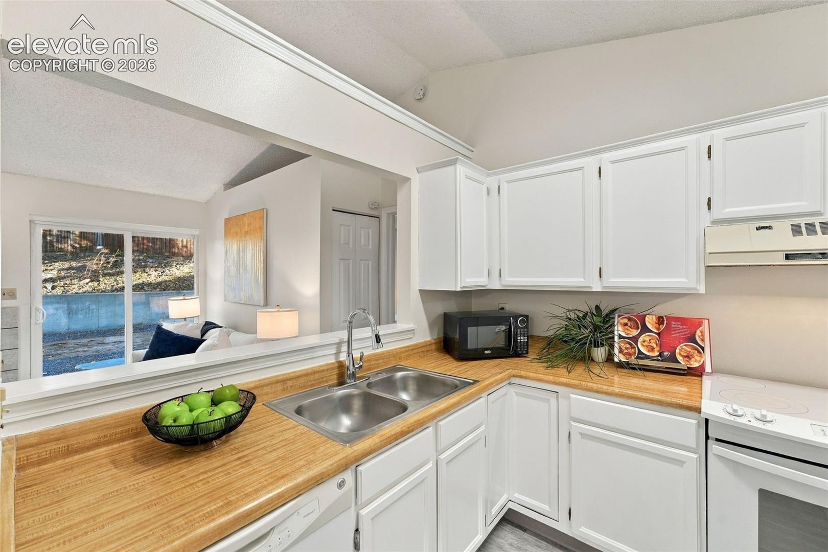 Kitchen featuring white cabinetry, butcher-block countertops, dual-basin stainless steel sink with high-arch faucet, and white electric range