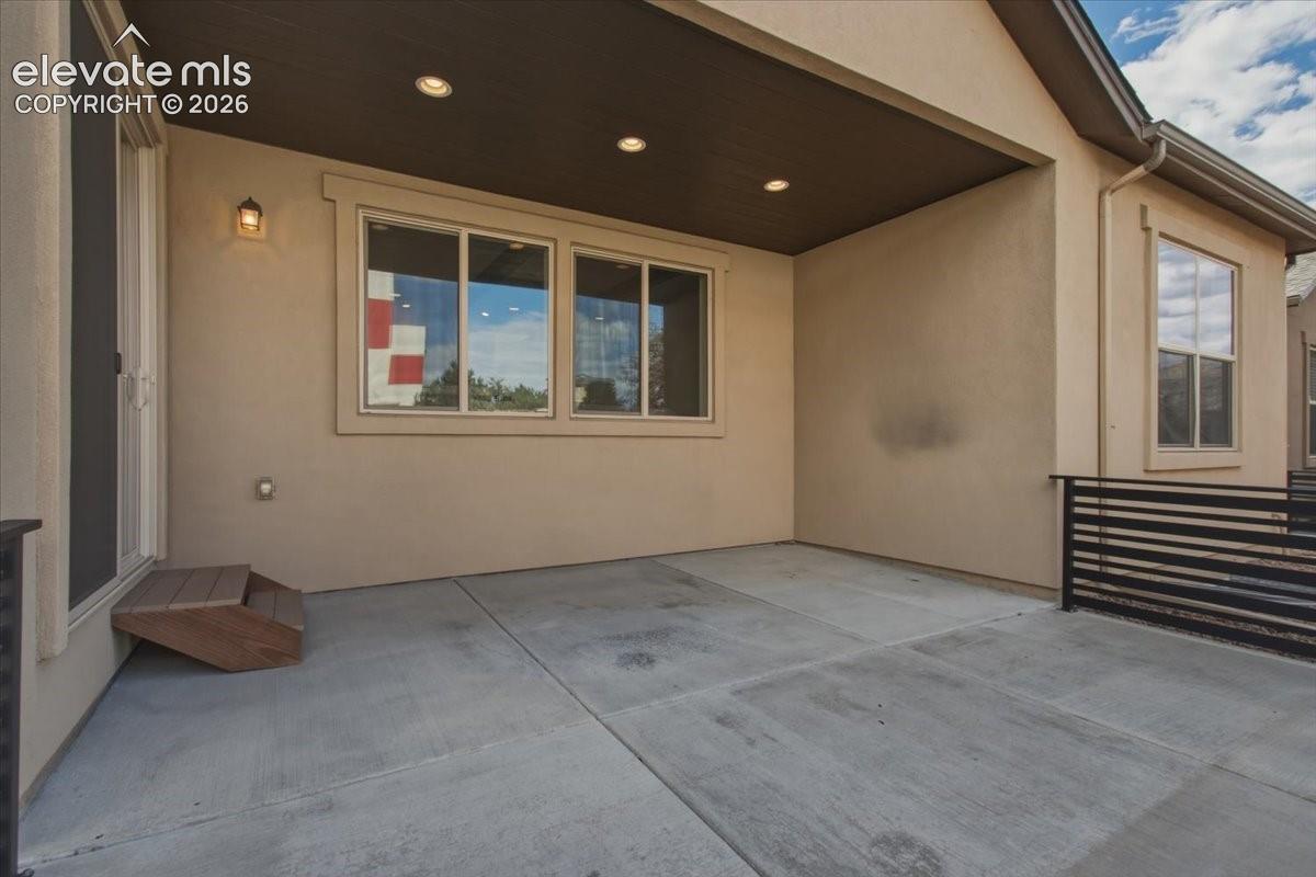 Covered concrete patio featuring recessed ceiling lighting, a dark wood-finish ceiling, and horizontal metal railing