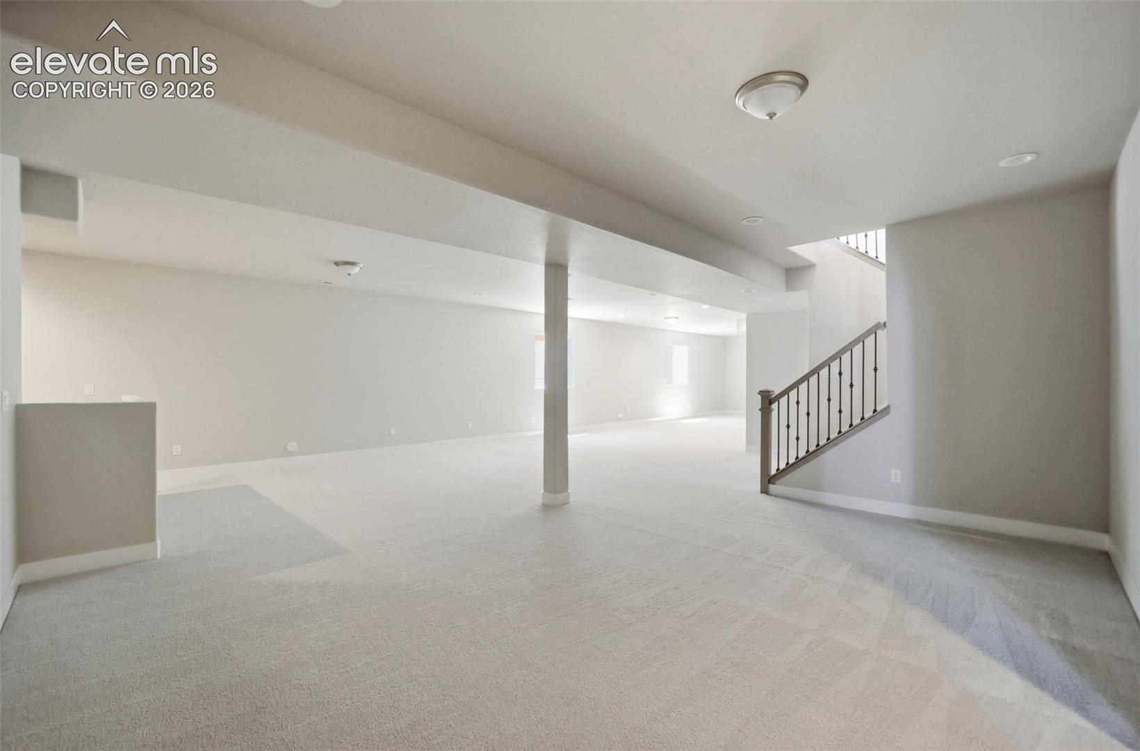 Expansive open-concept space featuring wall-to-wall carpeting, neutral interior paint, recessed lighting, and a staircase with decorative metal balusters