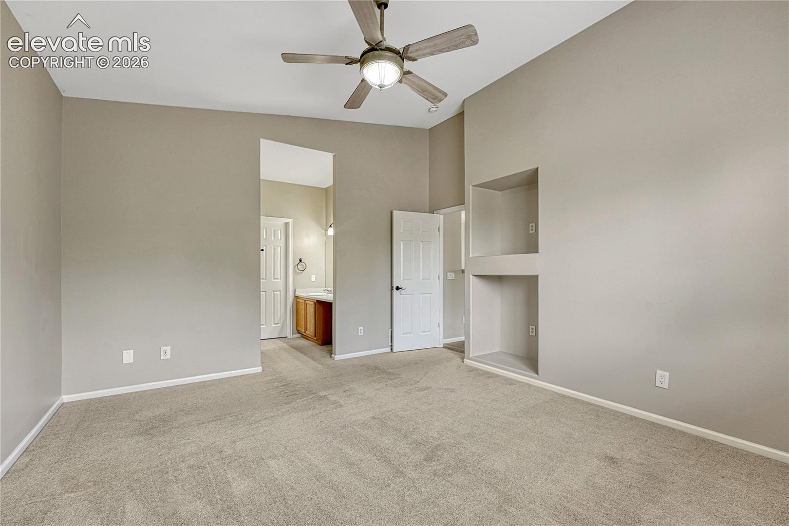 Vaulted ceiling with a central brushed-nickel ceiling fan, dual-level built-in recessed shelving, neutral wall coloring, and carpeting throughout